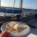 A freshly made apple crêpe dusted with powdered sugar, served on board a historic sailing ship during a sunny cruise.
