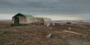 An expedition camp on the Arctic tundra in the Great Arctic State Nature Reserve, consisting of several field tents and research equipment. The camp overlooks the coastal plain of Knipovich Bay beneath a cloudy sky.