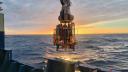 A CTD instrument being lowered into the ocean at sunset from the research vessel, with water sampling bottles and sensors visible.