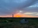 Twee tenten in het gras bij zonsondergang, met het historische navigatiebaken op de achtergrond.