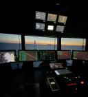 The darkened bridge of the research vessel Anna Weber-van Bosse, with multiple navigation and control screens overlooking the horizon at sunset.