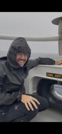 Samuele sits smiling in rain gear on the bow of the vessel, looking out to sea through an opening.