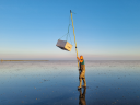 PhD candidate Evy Gobbens at work on the mudflats of the Wadden Sea: carrying part of her installation on a long stick.