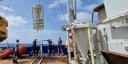 Crew on a research ship deploy a sediment trap labeled “TRAP KIEL” over the side using a crane.